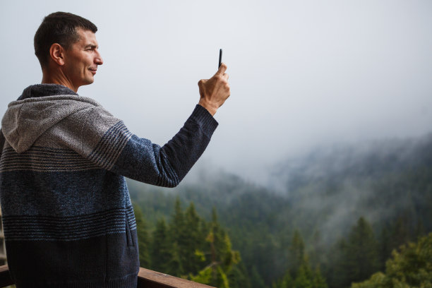 一位年轻人用手机拍摄酒店阳台上美丽的群山景色图片下载