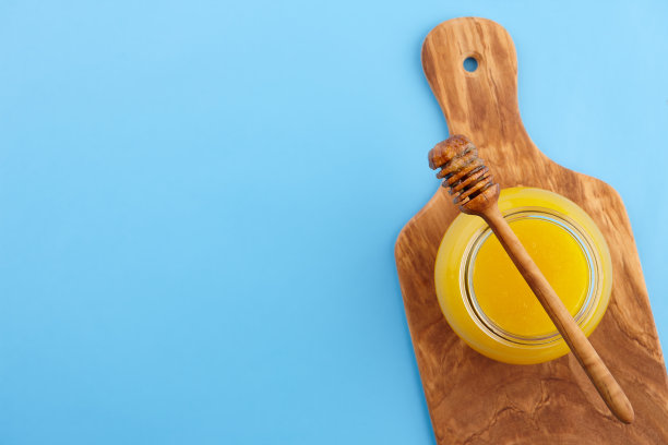 蓝色背景的切菜板上的蜂蜜罐图片下载