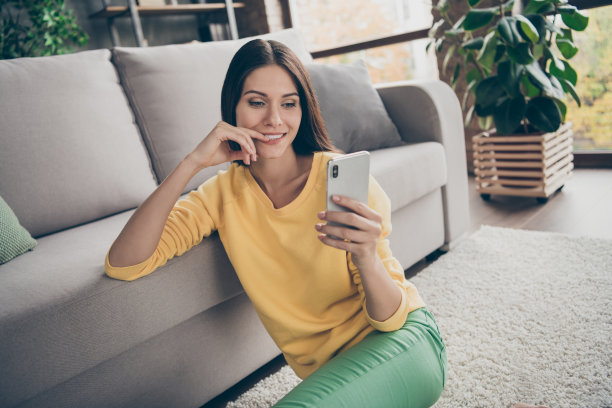 好奇的女学生坐在地板上用智能手机阅读社交媒体新闻的特写照片，在家里的客厅里思考，感觉灵感图片下载