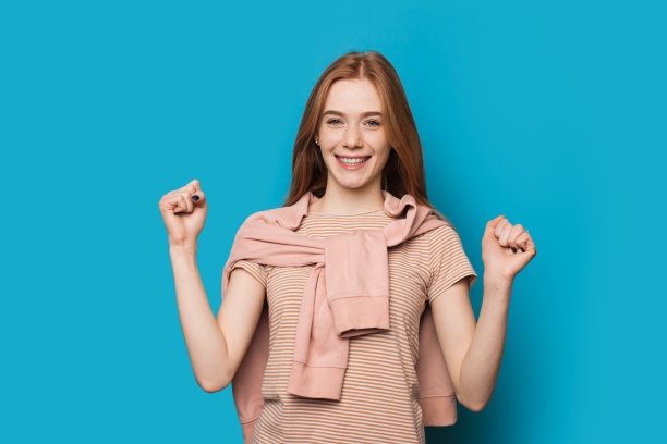 快乐的白人女性，红色头发和雀斑，在蓝色背景上用毛衣遮盖着力量标志图片下载