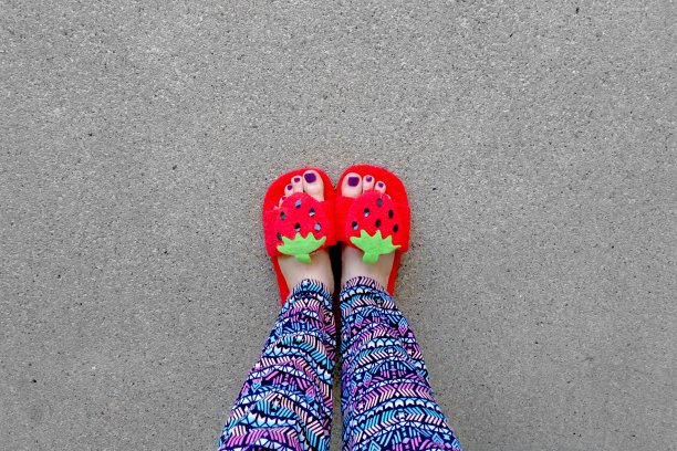 儿童拖鞋鞋地板背景，俯视图。漂亮的年轻女子，穿着草莓红凉鞋。清除暖和的家用鞋。从上面自拍脚和腿。图片下载
