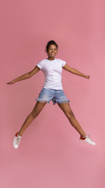 非洲少女跳跃与开放的双手在粉红色的背景图片下载