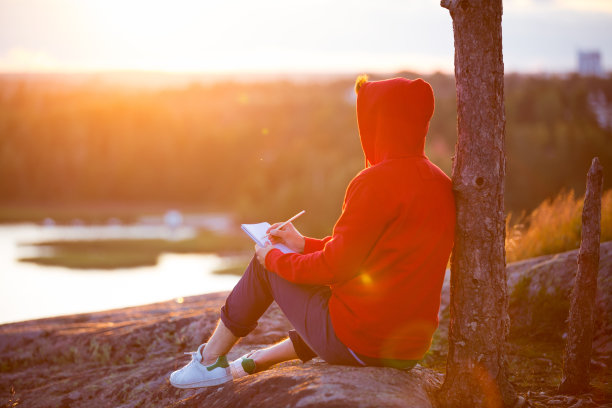 一个穿着帽衫的年轻人坐在岩石顶上图片下载