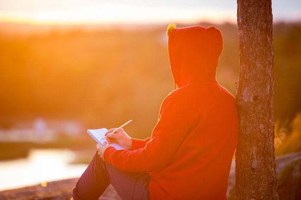 一个穿着帽衫的年轻人坐在岩石顶上图片下载