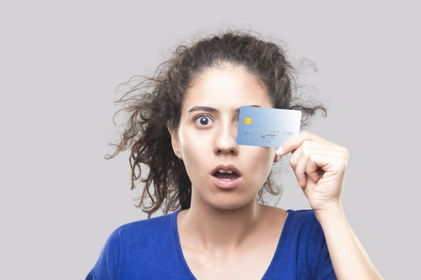 一个震惊的年轻女子的肖像，灰色的背景上有一张信用卡图片下载