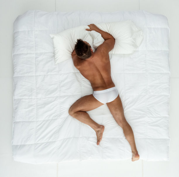 年轻男性穿着男士内裤在卧室的白色背景前休息图片下载