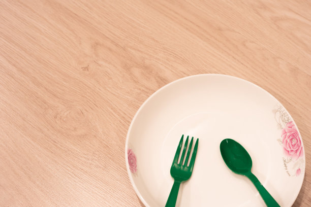 木地板上放着一个白色的盘子和绿色的塑料餐具图片下载
