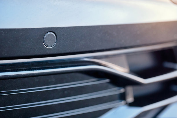 对豪华汽车保险杠前的停车辅助系统的停车传感器进行选择性聚焦，近距离观察灯光模糊的背景。图片下载