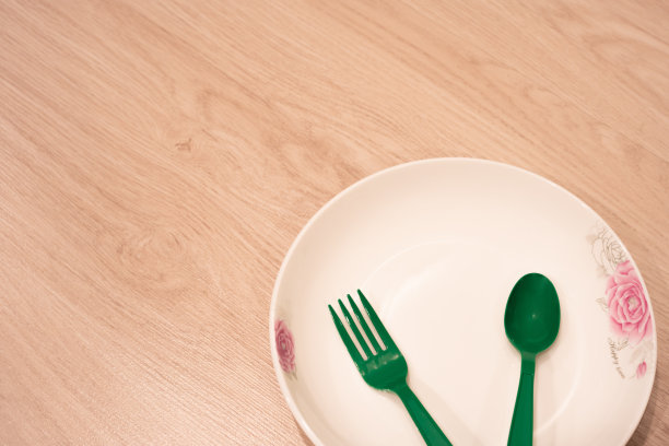 木地板上放着一个白色的盘子和绿色的塑料餐具图片下载