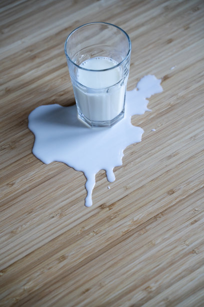 木桌上的玻璃杯和洒在水坑里的牛奶图片下载