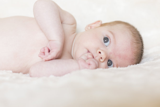 一个可爱的小女孩的肖像，醒着，看着相机。白色的毯子背景图片下载