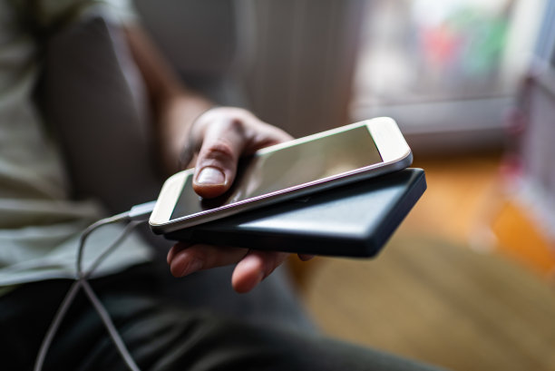 特写的年轻男子手持便携式充电器的智能手机图片下载