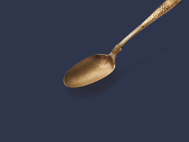 在空旷黑暗的地面上放着一个古老的金色勺子。图片下载