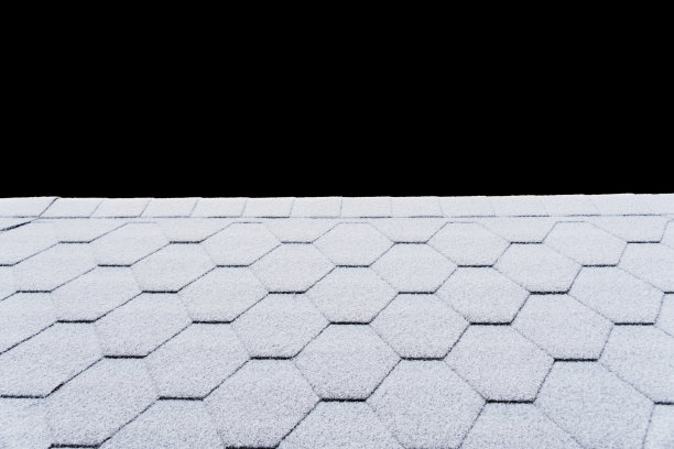 沥青屋面瓦片上覆盖着轻盈的积雪纹理。房屋的屋顶瓦片上覆盖着霜。被雪覆盖的屋顶被隔离在黑色背景和剪切路径上。图片下载