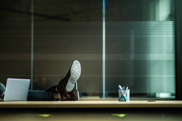 一个面目全的商人把脚搁在办公室的桌子上。图片下载