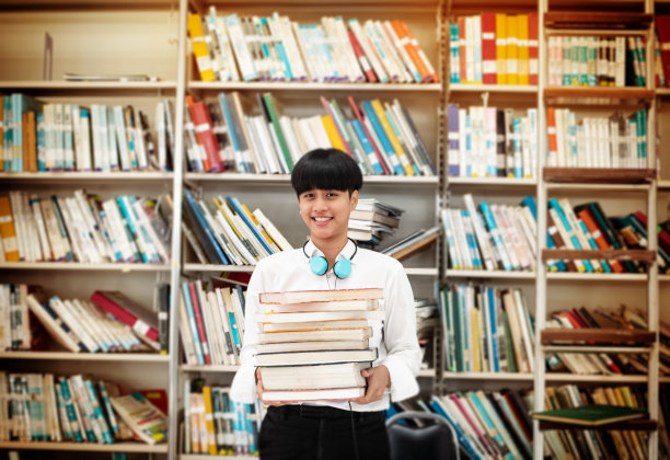 在图书馆手捧书籍查找资料的年轻少女图片下载