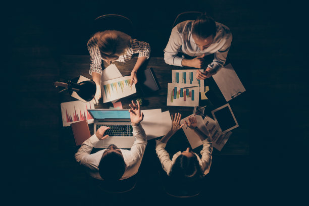 四位商务伙伴在桌旁工作至深夜讨论新创业公司正式服装台灯灯光室内高角度照片图片下载