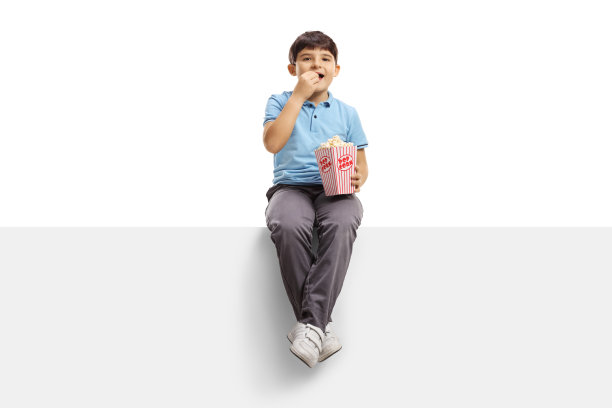 可爱的男孩坐在面板上吃着爆米花图片下载