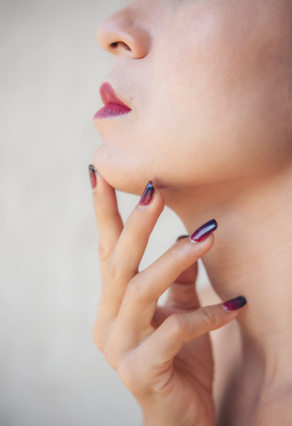 化着妆的亚洲美女：魅力女孩，红唇美甲，使用护肤粉底，面部在浅色背景上，时尚摄影概念图片下载