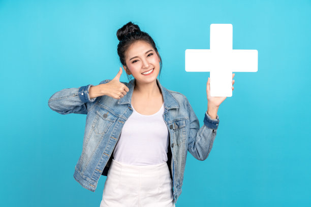 幸福亚洲女人微笑，显示加号或添加标志和拇指向上或喜欢在蓝色的背景。可爱的亚洲女孩穿着休闲牛仔裤衬衫和显示加入标志增加和更多的利益的概念图片下载
