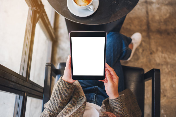 一位女士坐着并拿着带有空白白色桌面屏幕的黑色平板电脑图片下载