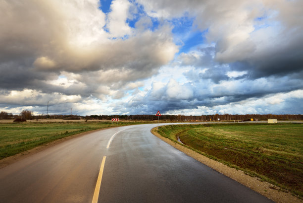 空旷的柏油路上空乌云密布。背景是农田和森林。晚上温暖的阳光。波罗的海，加尔希姆斯，拉脱维亚图片下载