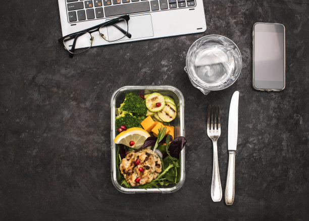 健康午餐盒容器烤鸡肉丸，花椰菜，西葫芦，南瓜和沙拉在黑色的背景。在办公室的工作场所健康饮食。图片下载