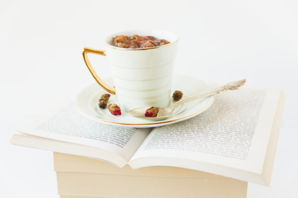 用杯子和勺子盛着玫瑰干茶。热饮上打开的书。白色背景。极简主义的风格。副本的空间。前视图。图片下载