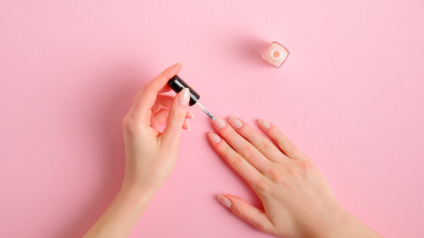女人在家涂指甲油。纤纤玉手涂着优雅的指甲油，粉色背景，俯视。美容护理和手部护理概念图片下载