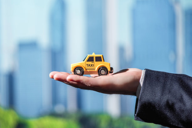在芝加哥摩天大楼的背景中，一个穿着西装的商人的手拿着一辆黄色的玩具出租车。的概念。城市出租车服务图片下载