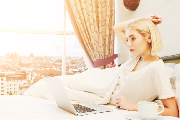 快乐的女人坐在酒店房间的床上图片下载