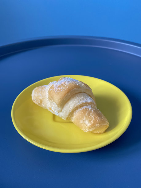 黄色的盘子与新鲜的羊角面包撒糖粉蓝色圆桌作为时尚的背景。手机照片图片下载