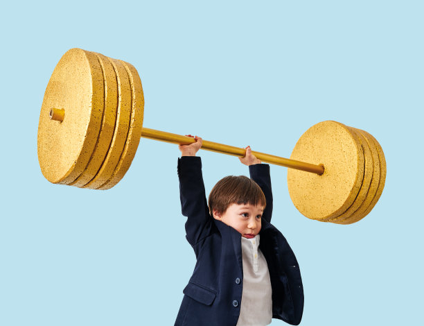 可爱的孩子举起金色的杠铃在蓝色柔和的背景。他是一个有决心和成功的孩子。图片下载