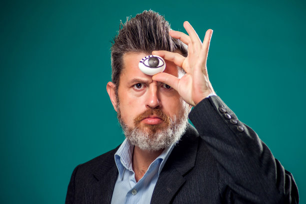 一幅男人的肖像，穿着西装拿着鸡蛋，眼睛靠近前额。第三只眼的概念图片下载