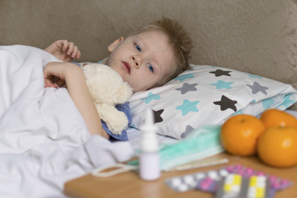 生病难受的孩子躺在床上，发烧头痛，旁边放着药物。流行性感冒病毒图片下载