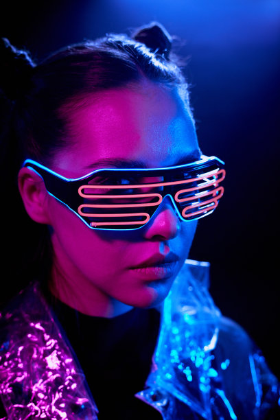 严肃的未来主义女孩的肖像，戴着霓虹丝护目镜站在蓝色的灯光下，在黑暗的房间里图片下载