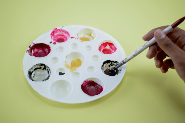 一个人用画笔从调色板上蘸取颜料，在黄色纸上绘画图片下载