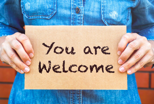 女人手里拿着一块硬纸板，上面写着:欢迎你以砖墙为背景。图片下载