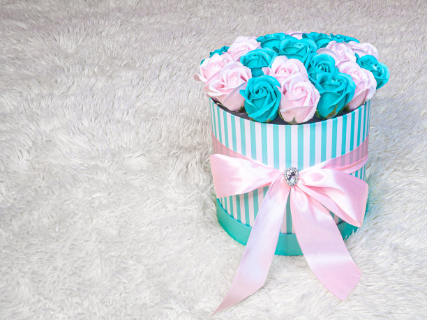 粉红色和绿松石玫瑰在圆柱形条纹礼盒与粉色丝绸丝带，在白色毛皮的背景。情人节和国际妇女节的图片。图片下载