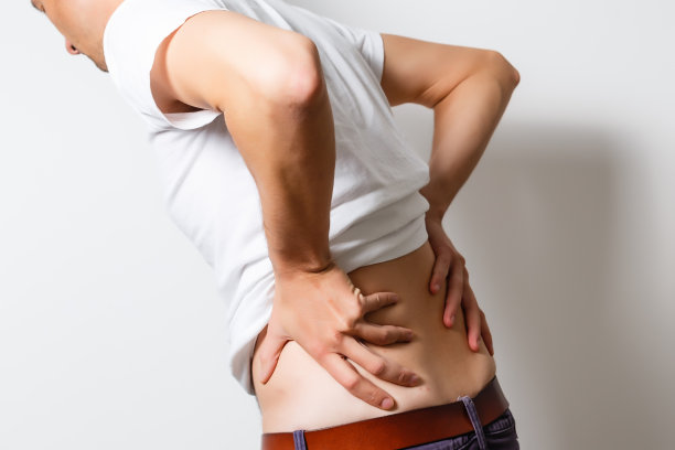 腰痛症状。年轻人握着发炎疼痛的腰部。保健和医药。图片下载