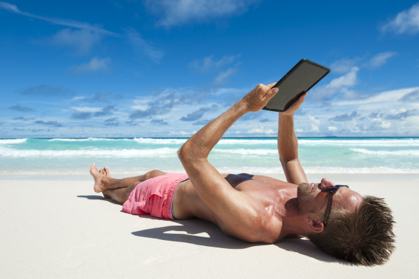 在海滩上用平板电脑放松的男人图片下载