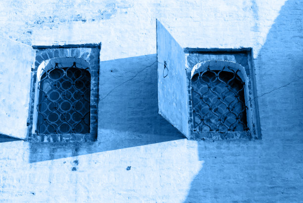 带有窗户的石墙，中世纪塔楼或城堡的立面片段，窗户上的格子和系泊，照片色调的经典蓝色单色，经典蓝色2020色图片下载