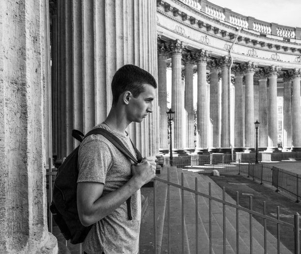 一个邪恶的年轻男子的侧面肖像与一个背包站在旁边的柱子喀山大教堂在圣彼得堡，黑白照片图片下载