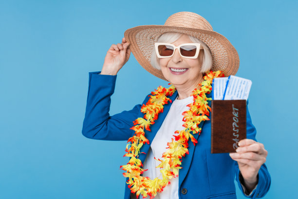 资深女性旅行者戴着太阳镜和帽子，拿着护照和机票孤立在蓝色背景图片下载
