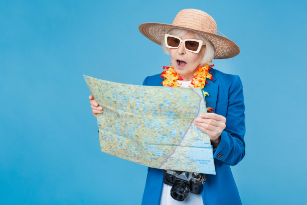 高级女旅行者拿着地图，看着它在蓝色的墙上孤立的点图片下载