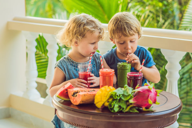 孩子们喝着色彩鲜艳的健康冰沙，西瓜、木瓜、芒果、菠菜和火龙果，各种冰沙、果汁、饮料和木桌上的新鲜水果图片下载