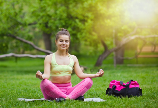 运动妇女在瑜伽姿势坐在一个垫子在公园的户外图片下载