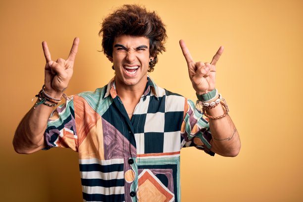年轻英俊的男人度假穿夏天的衬衫在孤立的黄色背景大喊与疯狂的表情做摇滚符号与手举起。音乐明星。沉重的概念。图片下载