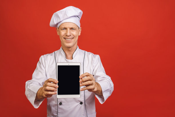 一个快乐的高级男厨师厨师显示空白平板电脑屏幕孤立在一个红色的背景。图片下载