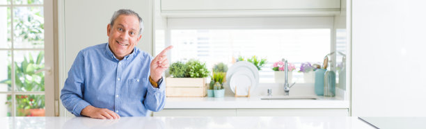 英俊老人居家微笑的广角照片，用手指着侧面看着镜头图片下载